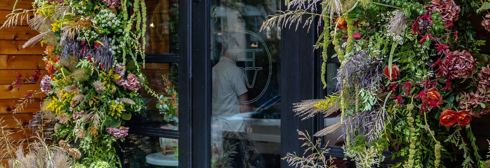 Restaurant entrance that is a glass door surrounded by an arrangement of Texas native plants. 