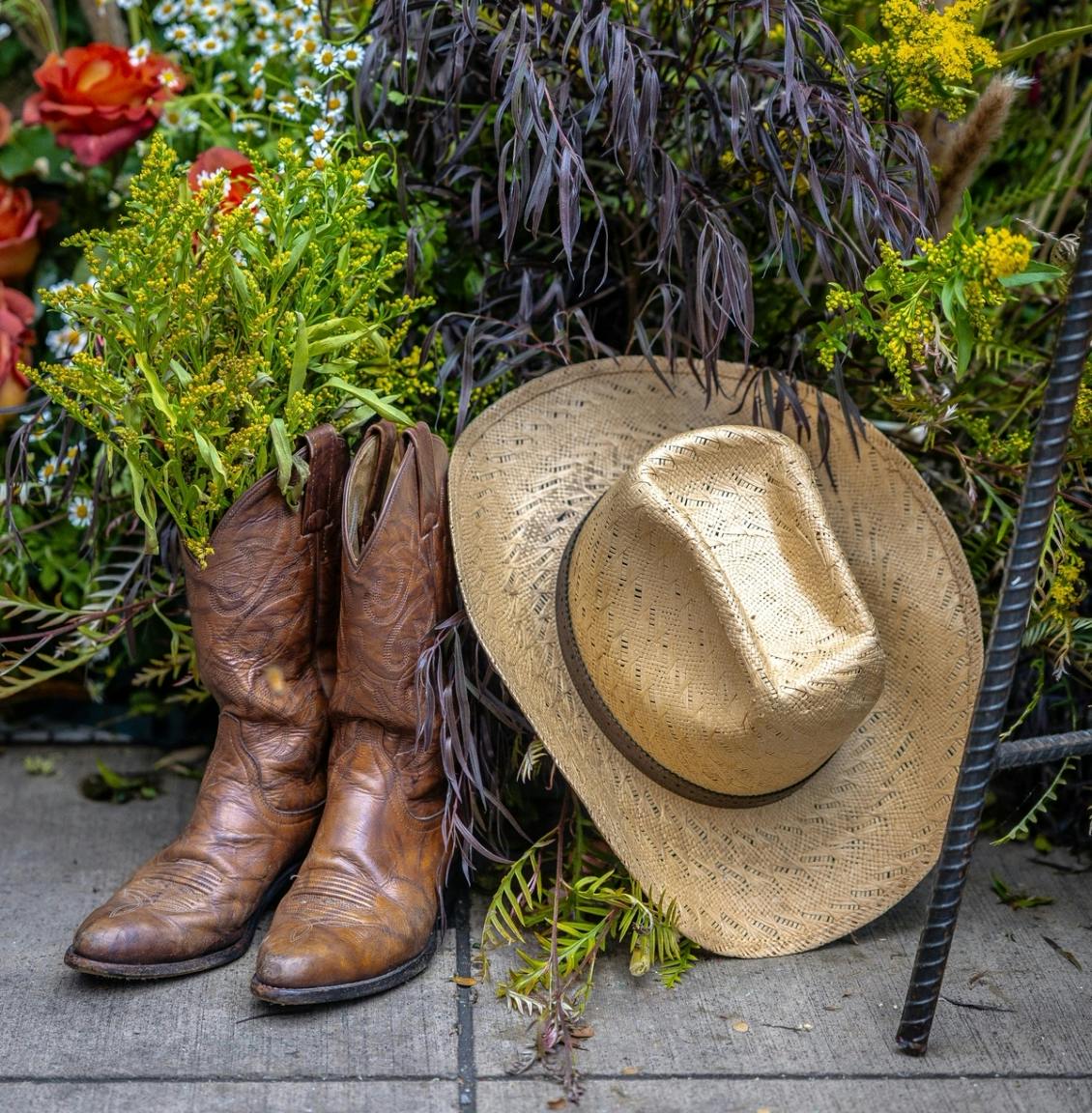 A pair of cowboy boots and hat leaned against a colorful bush. 